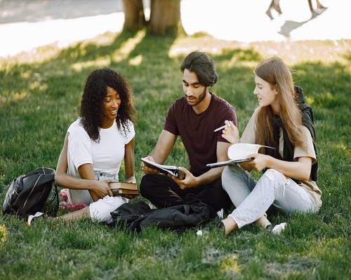 groupsmilinginternationalstudentssittinggrasstogetherparkuniversityafricancaucasiangirlsindianboytalkingoutdoors1scaled.jpg